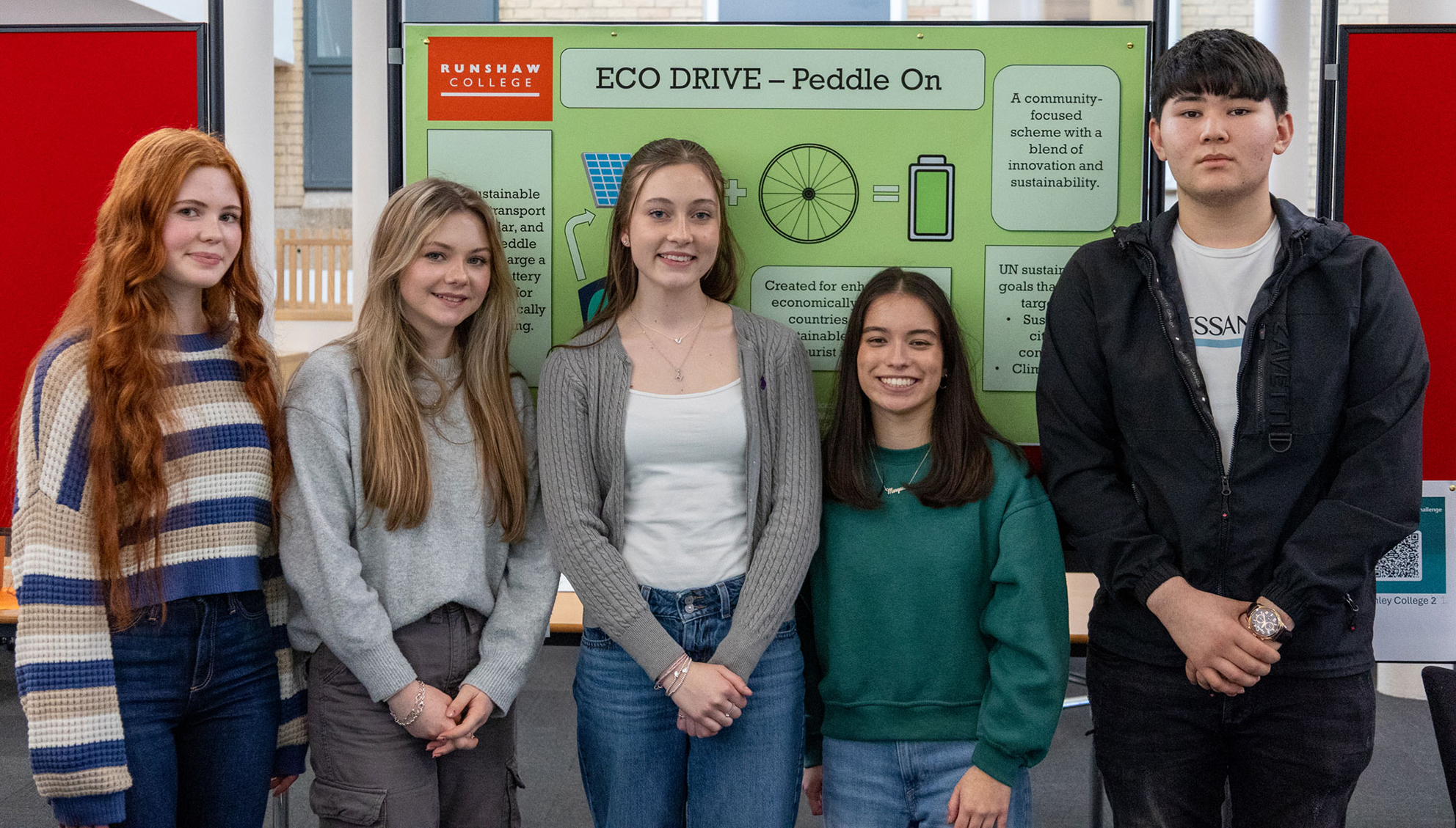 Four female college students and a male college student stand in a row in front of a green display panel with the words 'ECO DRIVE' written on it.