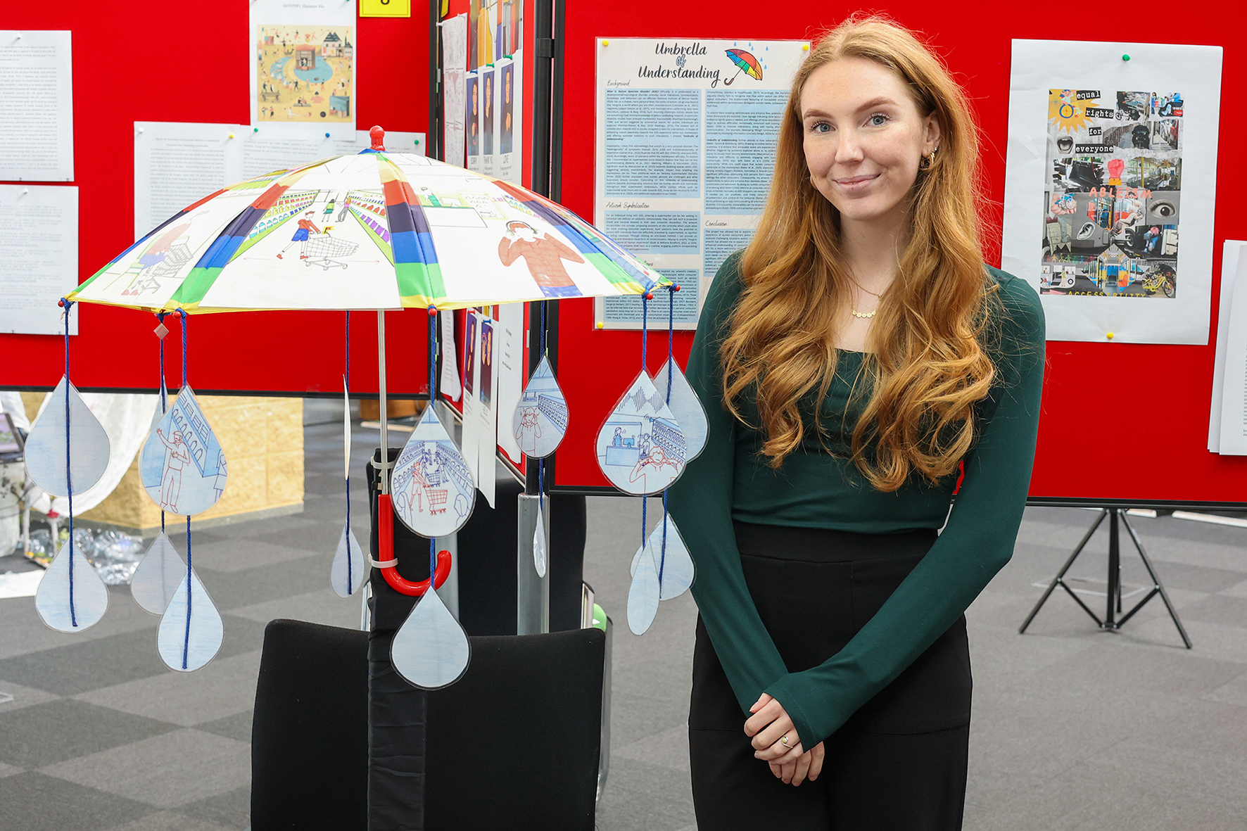 Student Leah Clayton stands with her artwork, an umbrella showing autistic experiences and solutions in supermarket settings
