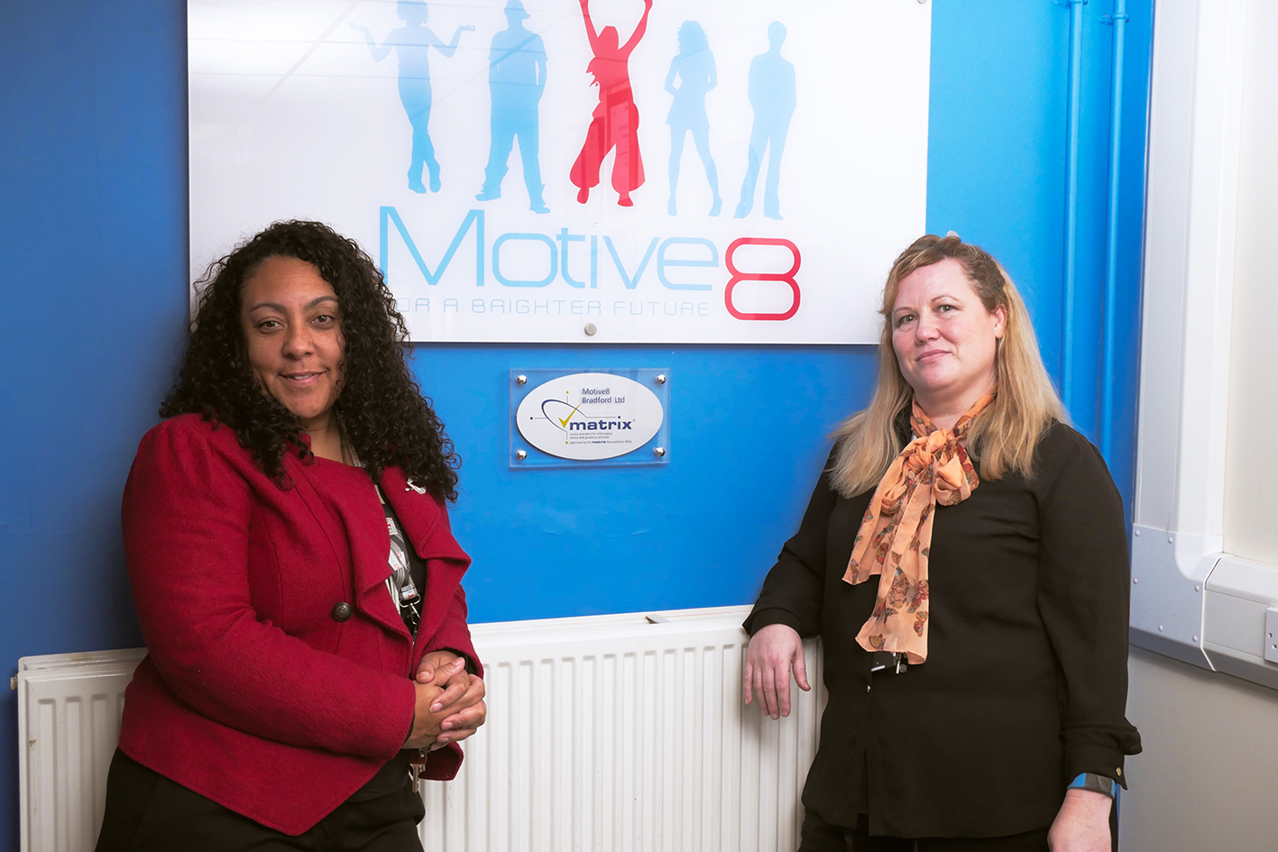 Motive8 Directors Melissa Simpson (left) and Moy Grange stand next to the Motive8 College logo