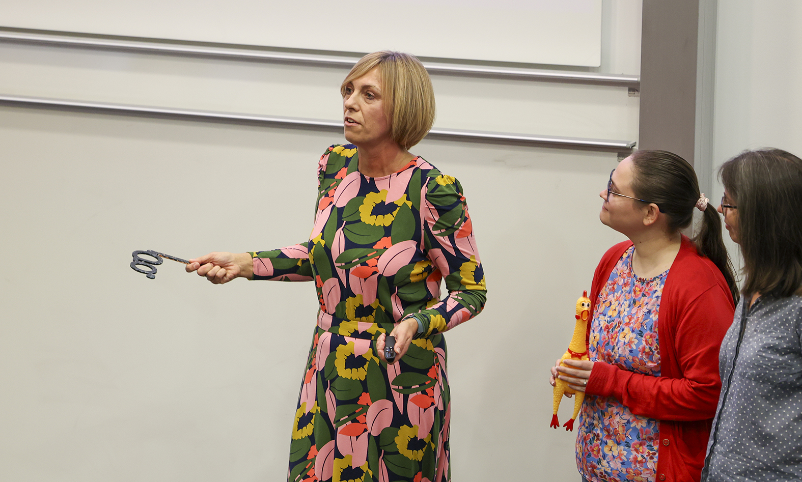 Dr Radka Newton gives her Perfect Pitch presentation while holding an opera glasses prop. Colleague Dr Jenni Carter stands watching holding a yellow rubber chicken prop.