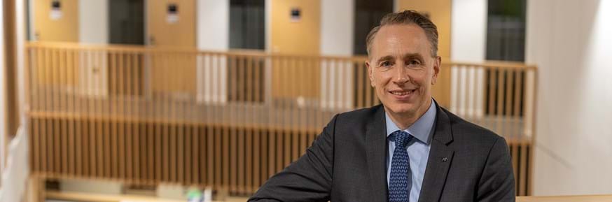 Thomas Buberl leaning against a wooden bannister in Lancaster University Management School