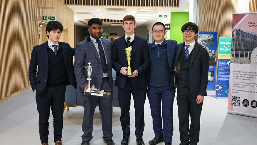 Five young men wearing suits stand shoulder to shoulder while holding trophies for winning a competition.