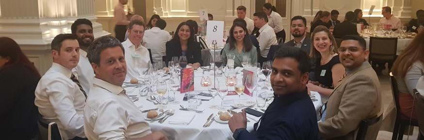 Students and alumni from the Lancaster MBA sit smiling around a table with dinner settings