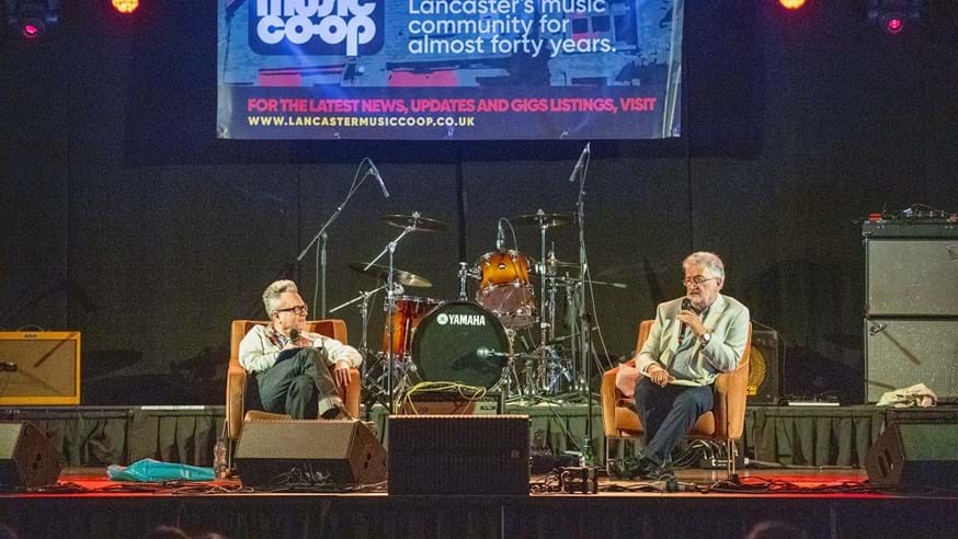 Two men sitting in armchairs talking on stage