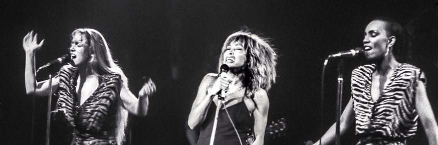 Black and white image of Tina Turner on stage with backing singers