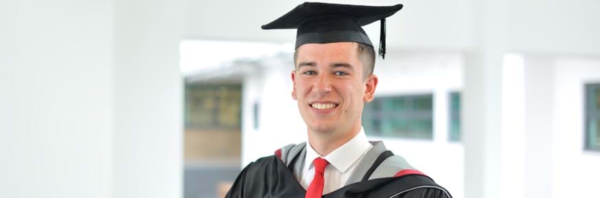 Ben Teague smiling in Lancaster Environment Centre wearing his black, red and grey graduation gowns