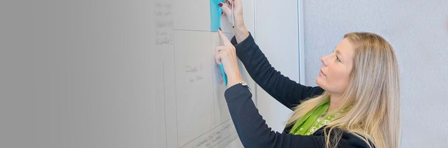 A woman sticking a post it note onto a whiteboard