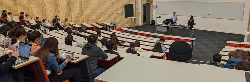 Paul McCormick and Tanya Parry deliver a session on internship placements. They are stood at the front of a large lecture theatre, in front of a big screen, with students sitting in front of them in rows making notes