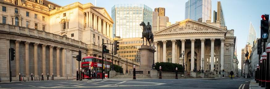 Panoramic view of the Bank of England and the Royal Exchange building in the City of London, with a red double decker bus passing nearby