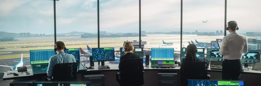 air traffic controllers working in a modern airport tower with aeroplanes on runways in the background