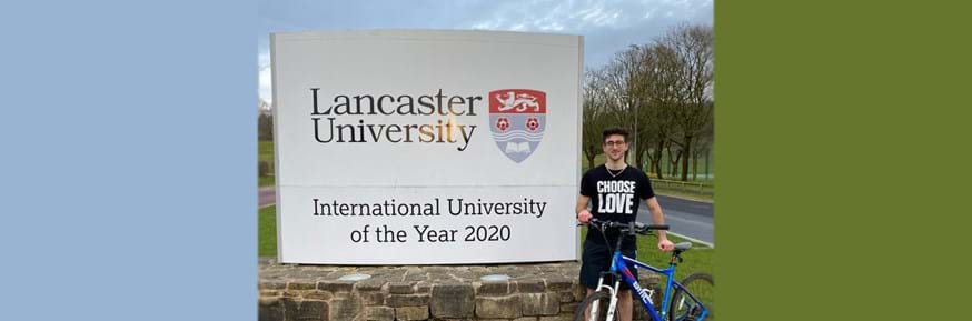 Aladdin Aljian with his bicycle in front of the Lancaster University sign at the campus entrance