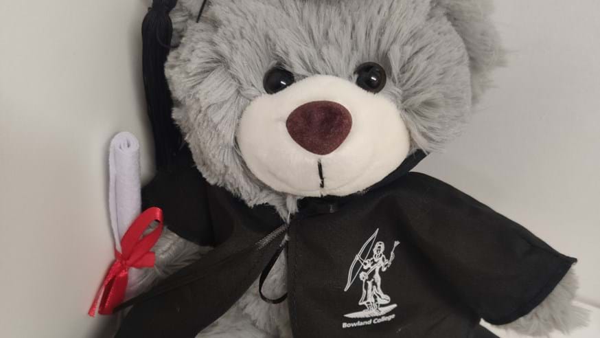 Grey bear wearing black gown with Bowland Lady logo printed in white, black mortar board and holding a scroll.