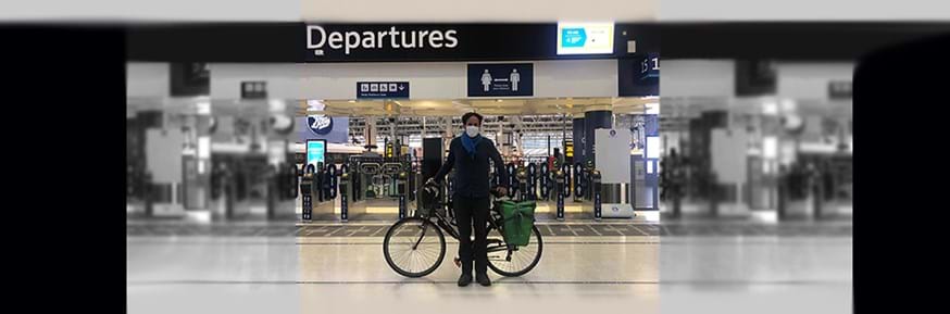 Dr Carlos López Galviz with his bicycle in front of a departures sign at a railway station ticket control
