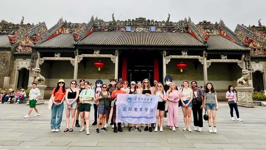 A group of people stood smiling at the camera outside the Chen Ancestral Temple in Guangzhou, China. Four people in the middle of the group are holding a sign that says 'School of International Education'.