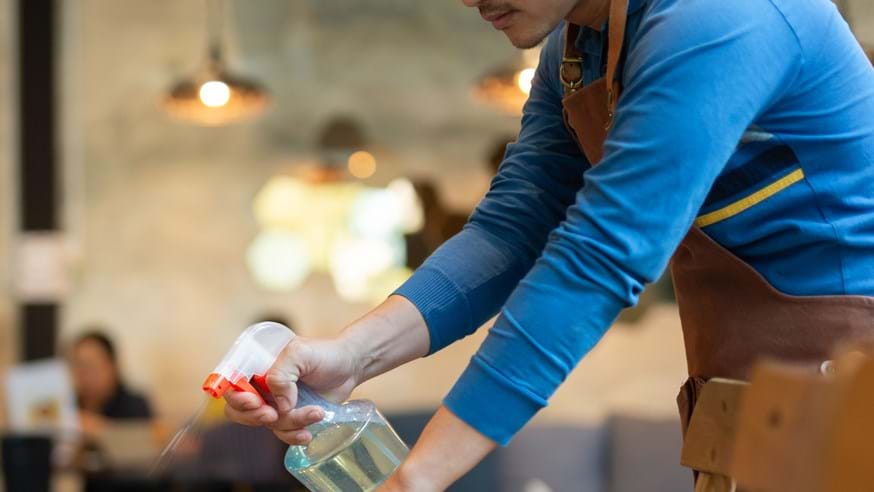Waiter cleaning a table in a restaurant with spray disinfectant.