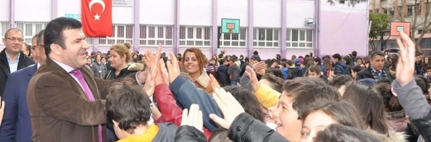 In a school playground smiling Dr Hasan Tanriseven shares 'high fives' with students beneath a Turkish flag