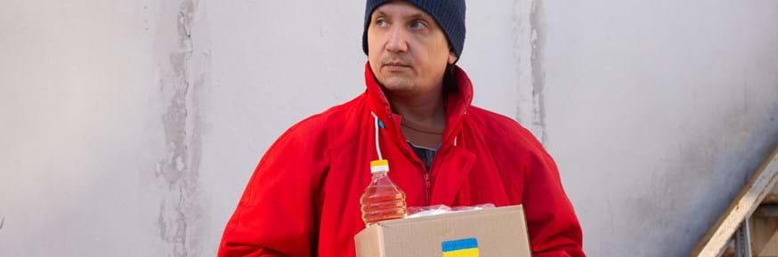 A charity worker in Ukraine holding a cardboard box with supplies in it