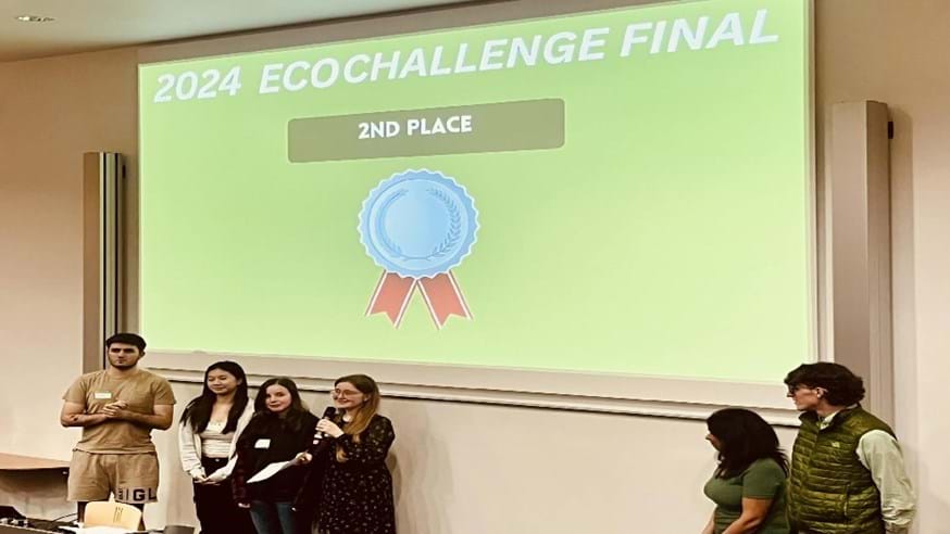 Furness and Fylde team members stood in a line in front of a large screen showing second place for the 2024 EcoChallenge Final
