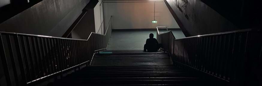 Person sitting at the bottom of a dark staircase