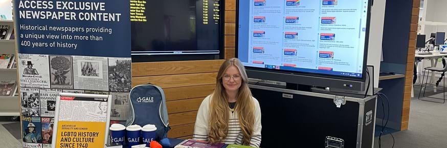 A photograph of Gale Student Ambassador, Georgia Winrow at Lancaster University Library. Georgia is at a desk with numerous information resources, and a Gale pull up banner.