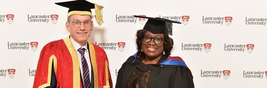 Vice-Chancellor Professor Andy Schofield with Funke Amobi dressed in their gowns for the graduation ceremony, holding Funke's award