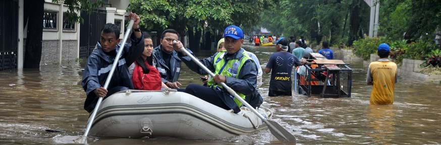 Rescuers paddle a rubber dinghy carrying people rescued from their homes down a flooded street in Indonesia