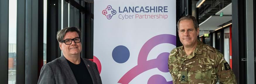 Two men standing either side of a poster reading 'Lancashire Cyber Partnership', smiling at camera