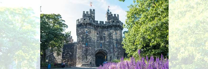 Lancaster Castle in the summer with purple flowers in the foreground