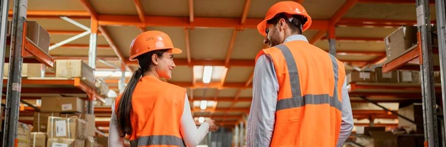 Image of a man and woman in high vis clothing wearing hard hats working in a warehouse
