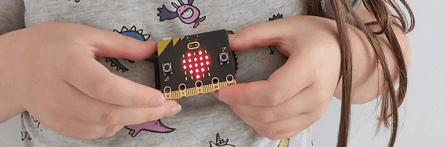 A girl holding a micro:bit displaying a heart