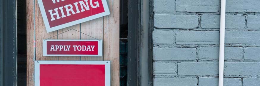 Image of a door with two red signs with white writing - 'we are hiring' and 'apply today'