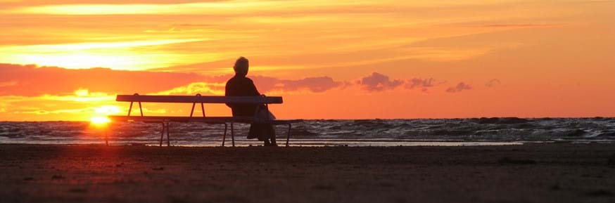 Elderly person alone sitting on a bench watching the sunset