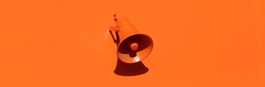 Orange megaphone attached to an orange wall.