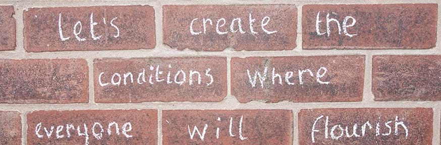 Brick wall with chalk writing saying: Let's create the conditions where everyone will flourish