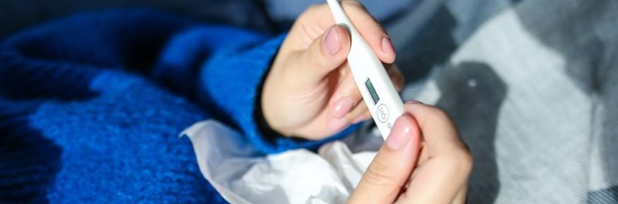 A person in a blue jumper holds a thermometer and a tissue