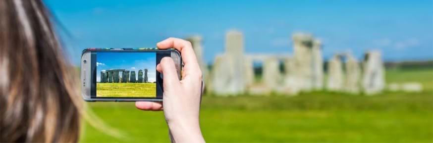 A woman takes a photo of Stonehenge on her phone.