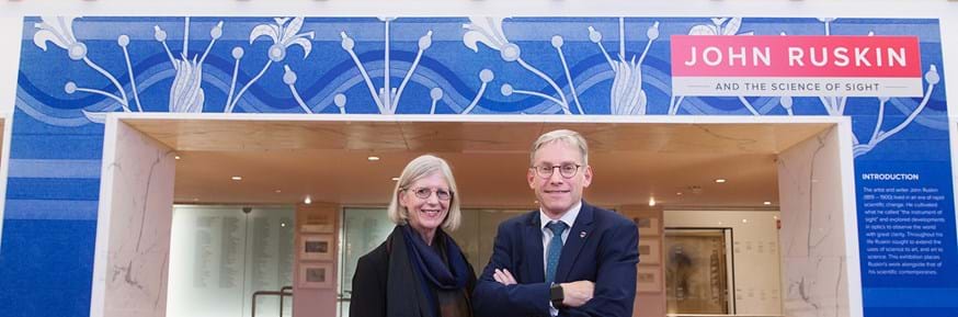Professor Sandra Kemp and Vice-Chancellor Professor Andy Schofield stand in front of a bannered archway bearing the words 'John Ruskin - And the Science of Sight'