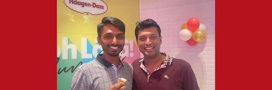 Rohit Murthy (left), holding an ice-cream cone, and Mayank Podar stand smiling in front of a sign saying Häagen-Dazs and a wall with balloons.
