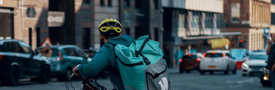 Deliveroo rider waiting at a junction on a busy road