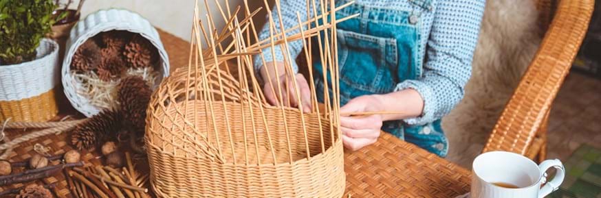 Image of a woman weaving a basket by hand on a table top