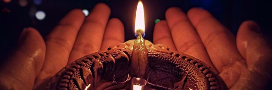Lighted candle on brown circle pot, being held in two hands.