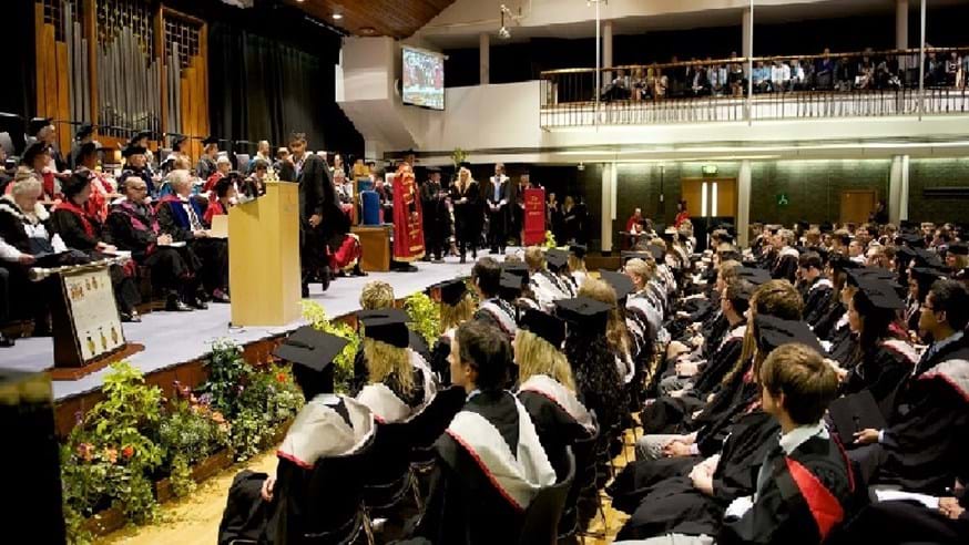 Photograph of a graduation ceremony in the Great Hall, with graduates seating in lines watching students collect their awards on the stage.