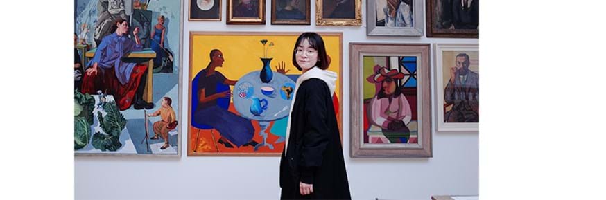 A female student standing in front of a wall of paintings in a gallery