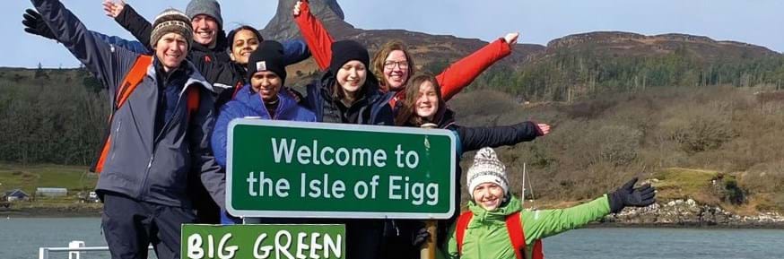 The Green Lancaster student teampose alongside a Welcome to the Isle of Eigg highway sign