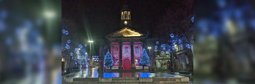 A photo of Lancaster Town Hall at night, lit up by the Christmas lights around it.
