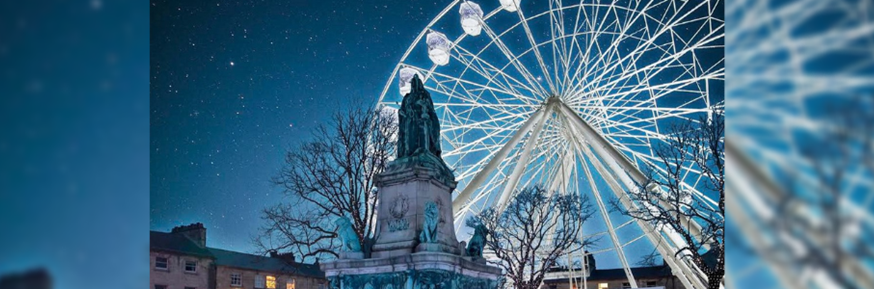 A photo of Dalton Square on a starry night. The Queen Victoria Monument stands in the foreground, with the ferris wheel in the background.