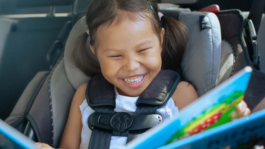 Little girl in a car seat reading a book - happy smile on face