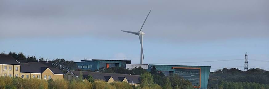 An image of Lancaster University campus, showing InfoLab in the foreground and the wind turbine behind