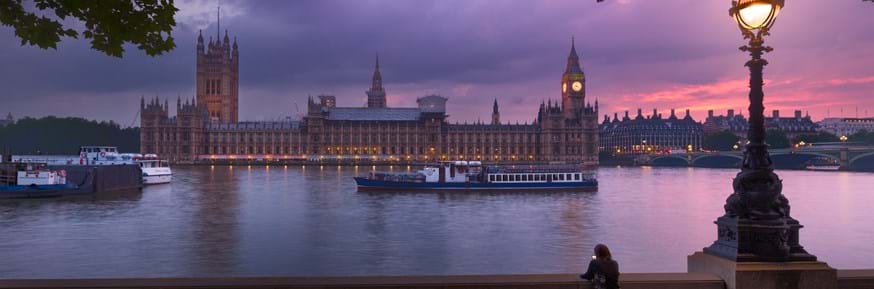 An image of the Houses of Parliament as seen from the opposite side of the Thames river, when the sun is setting.