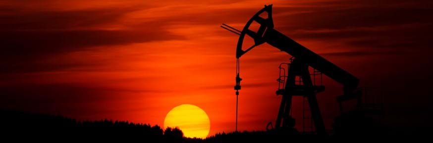An oil well operating in the desert in front of the setting sun